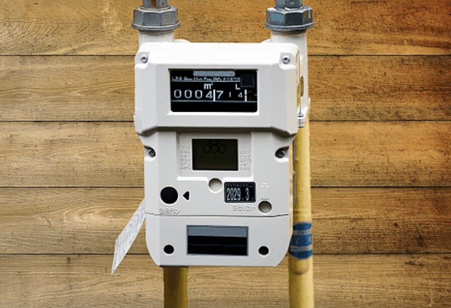 ガスメーター本体が配管に接続され、木目の壁の前に設置されている様子