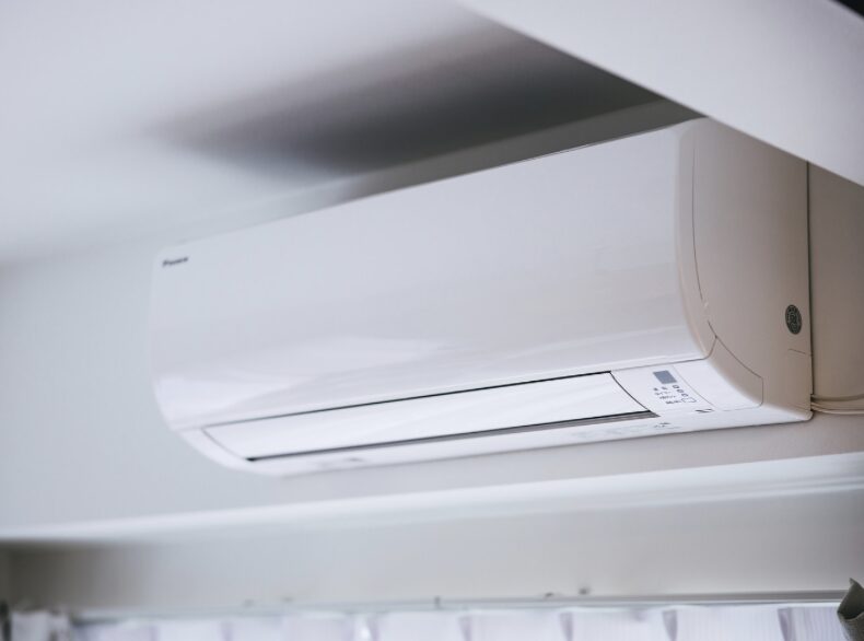 室内の壁上部に設置された白い壁掛けエアコンを斜め下から捉えたシンプルで明るい室内イメージ