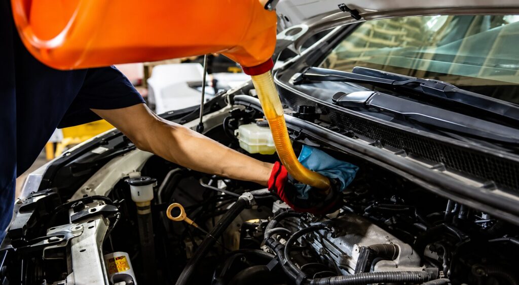 車のボンネットを開け、オレンジ色のオイル容器からエンジンへオイルを注入している整備作業の様子