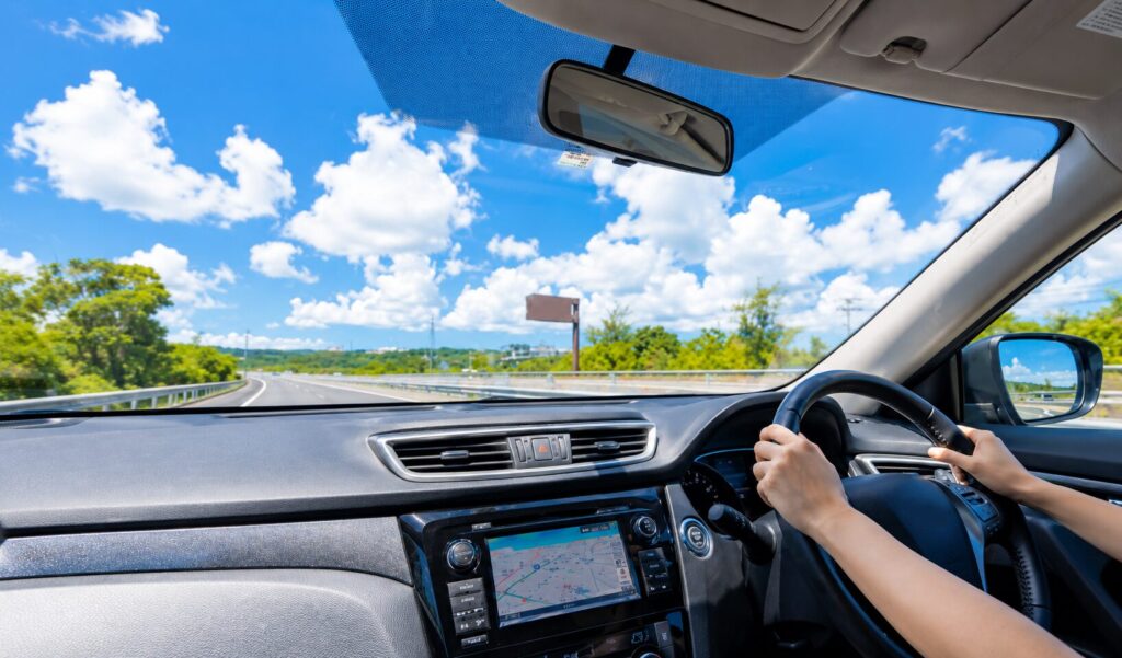 青空の下で高速道路を走行する車内からの風景とハンドルを握るドライバーの様子